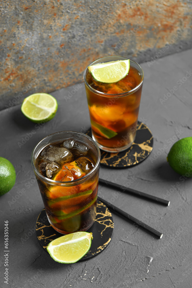 Glasses of cold Cuba Libre cocktail and limes on grey table