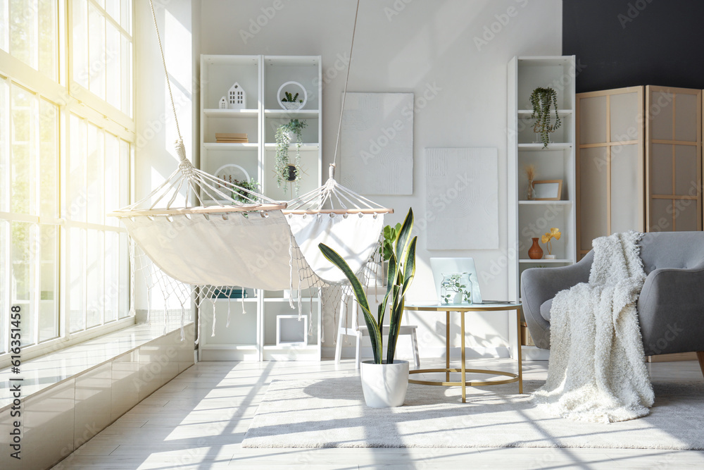 Interior of light living room with hammock, table and armchair