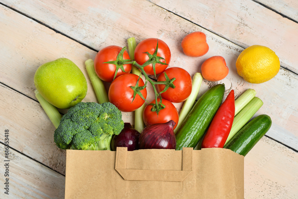 Paper bag with fresh vegetables and fruits on light wooden background