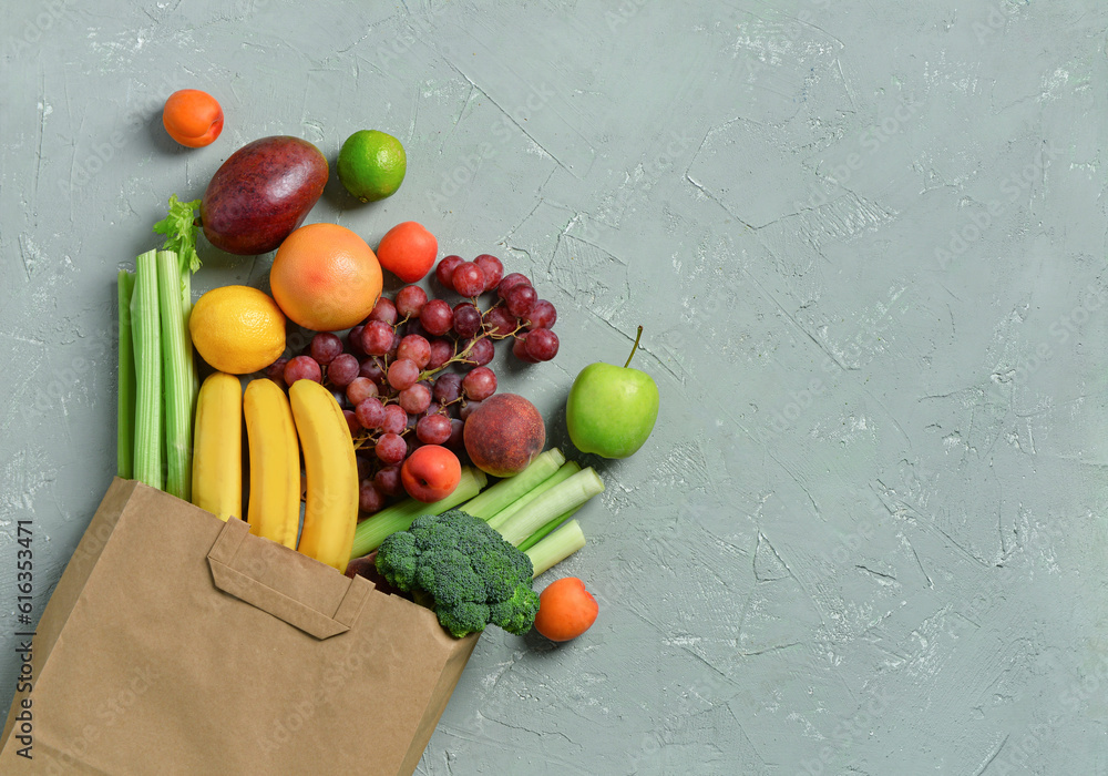 Paper bag with fresh vegetables and fruits on grey background