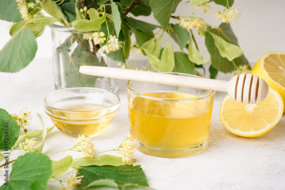 Glass bowl and plate of linden honey and dipper with fresh linden flowers on light background