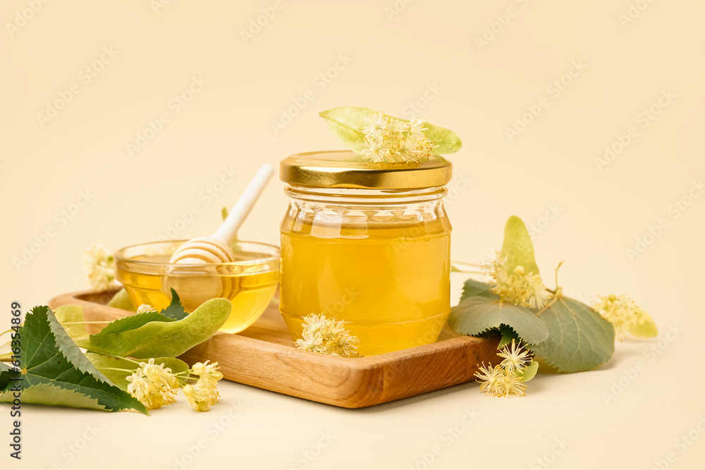 Wooden board with glass bowl and jar of linden honey on light background