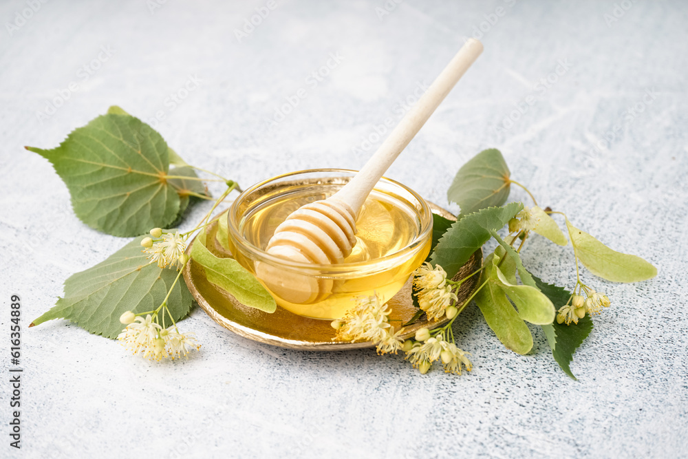 Plate with glass bowl of linden honey and dipper on grey background