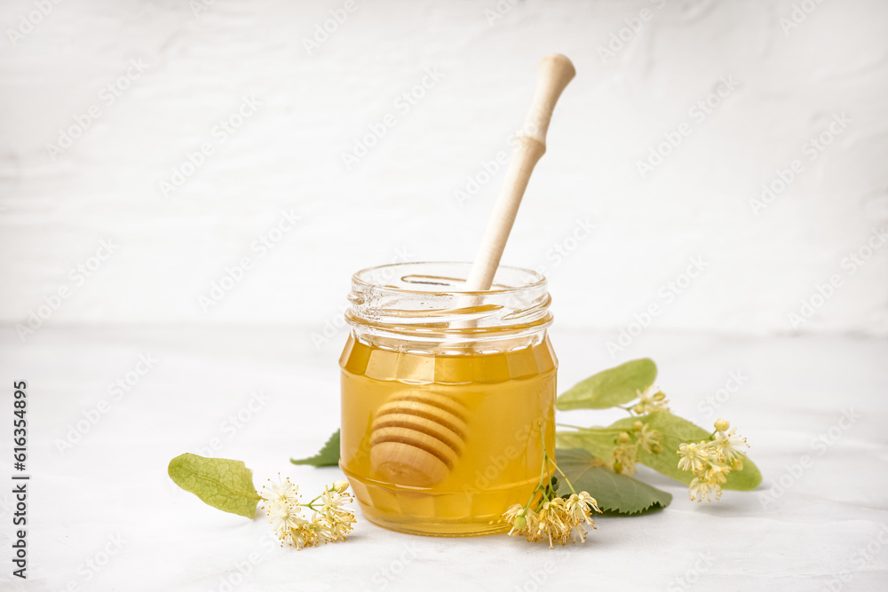 Jar with linden honey and dipper on white background