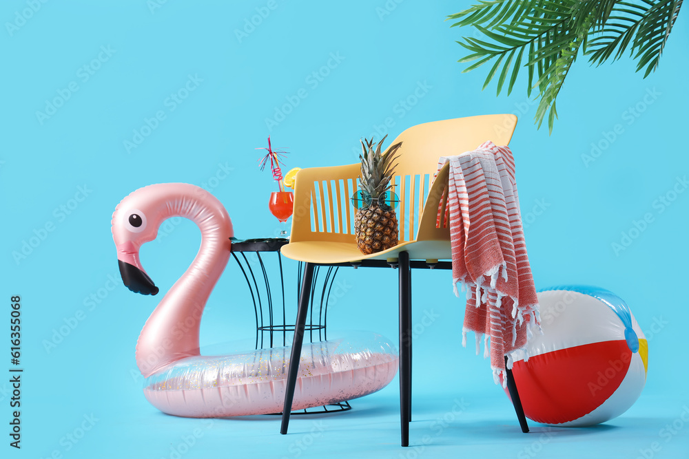 Composition with chair, pineapple, beach accessories and cocktail on table against blue background. 