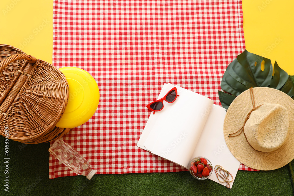 Basket with bowl of fresh strawberry for picnic, notebook and beach accessories on green grass again