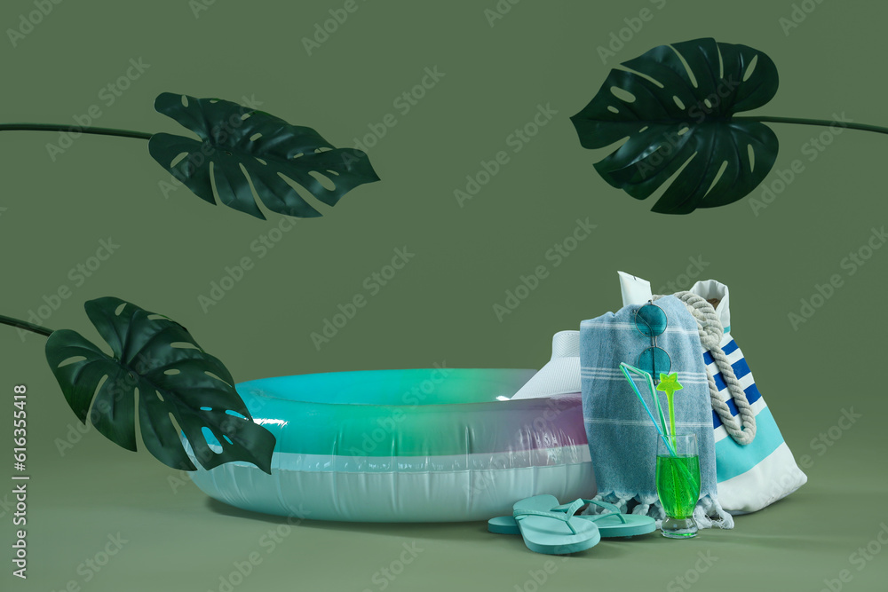 Inflatable ring with cocktail, palm leaves and beach accessories on green background. Travel concept