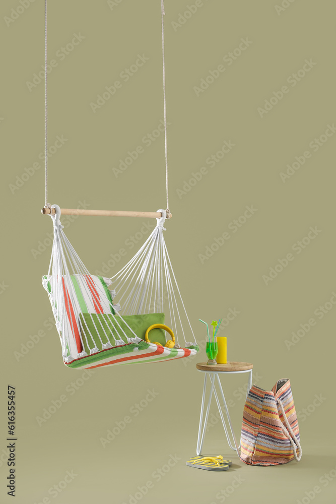 Hanging hammock with beach accessories and cocktail on stool against green background. Travel concep