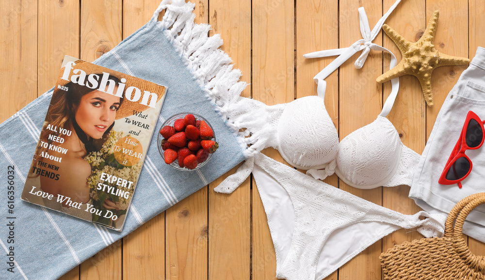 Bowl of strawberry with clothes, beach accessories and mobile phone on wooden pontoon against green 