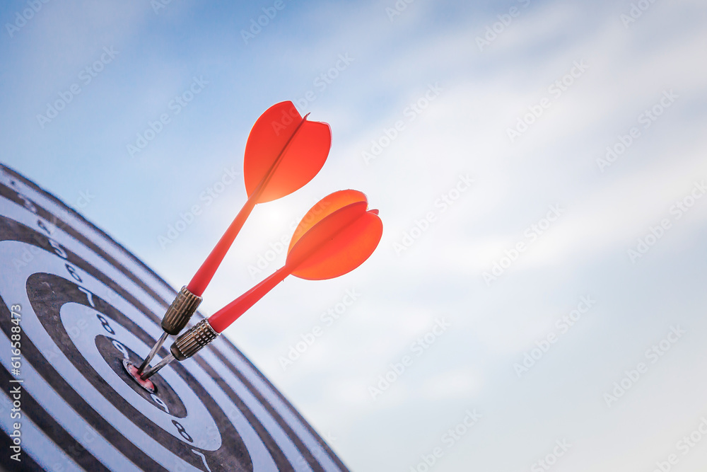 Close up shot red darts arrows in the target  of dartboard center on dark blue sky background. Busin