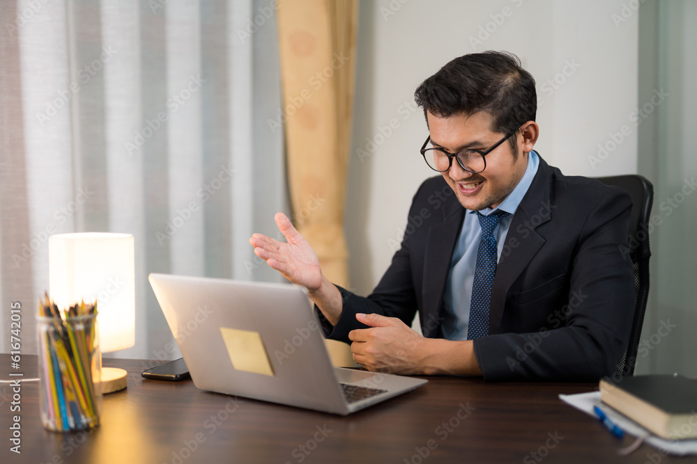 Happy young businessman sitting and discussing online meeting with laptop in private office.