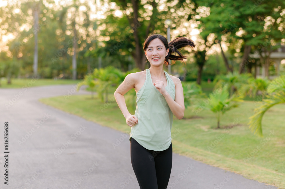 Fit Asian young woman jogging in park smiling happy running and enjoying a healthy outdoor lifestyle