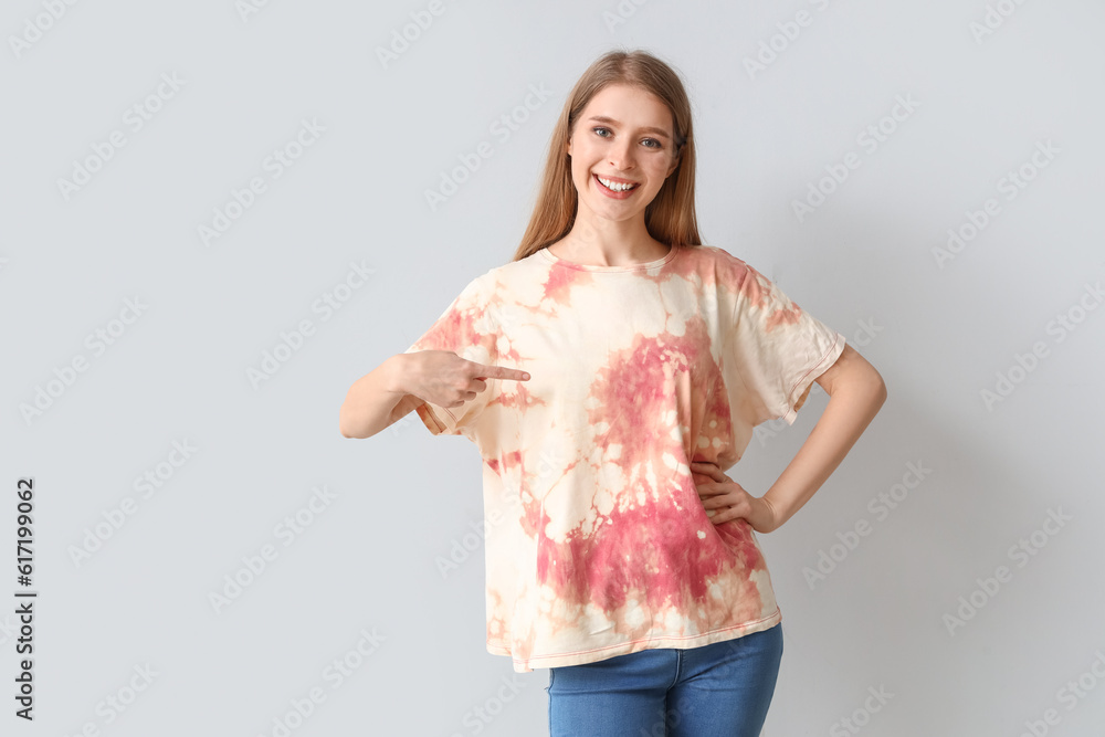 Young woman pointing at tie-dye t-shirt on light background