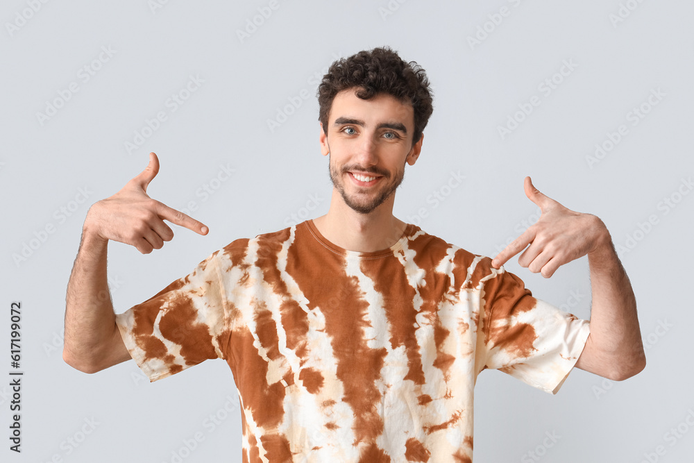 Handsome man pointing at tie-dye t-shirt on light background