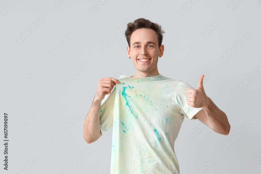 Young man in tie-dye t-shirt showing thumb-up on light background