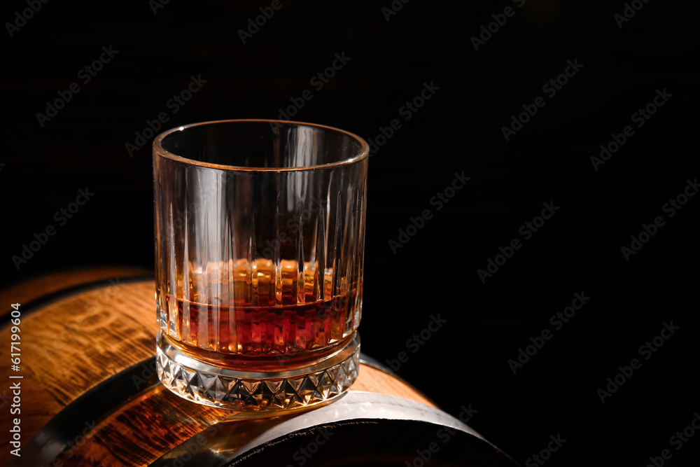 Barrel with glass of rum on black background