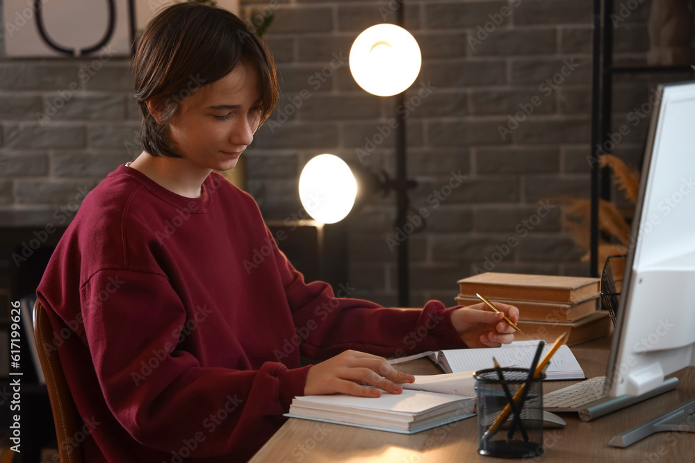 Teenage boy taking notes while reading book at table late in evening