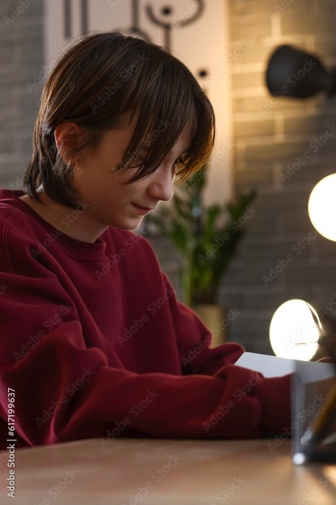 Teenage boy reading book at table late in evening, closeup