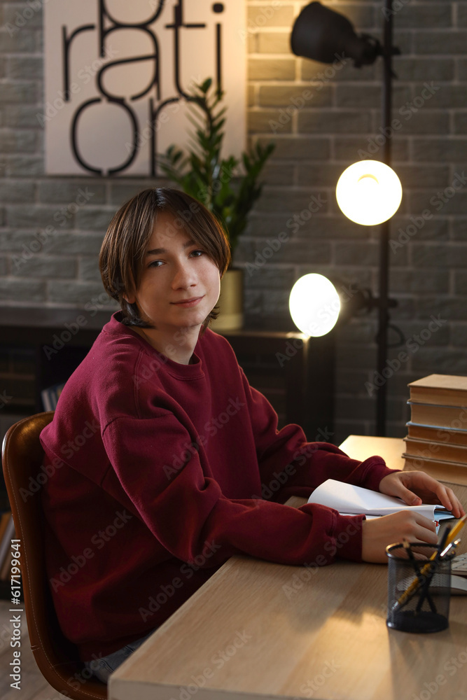 Teenage boy reading book at table late in evening