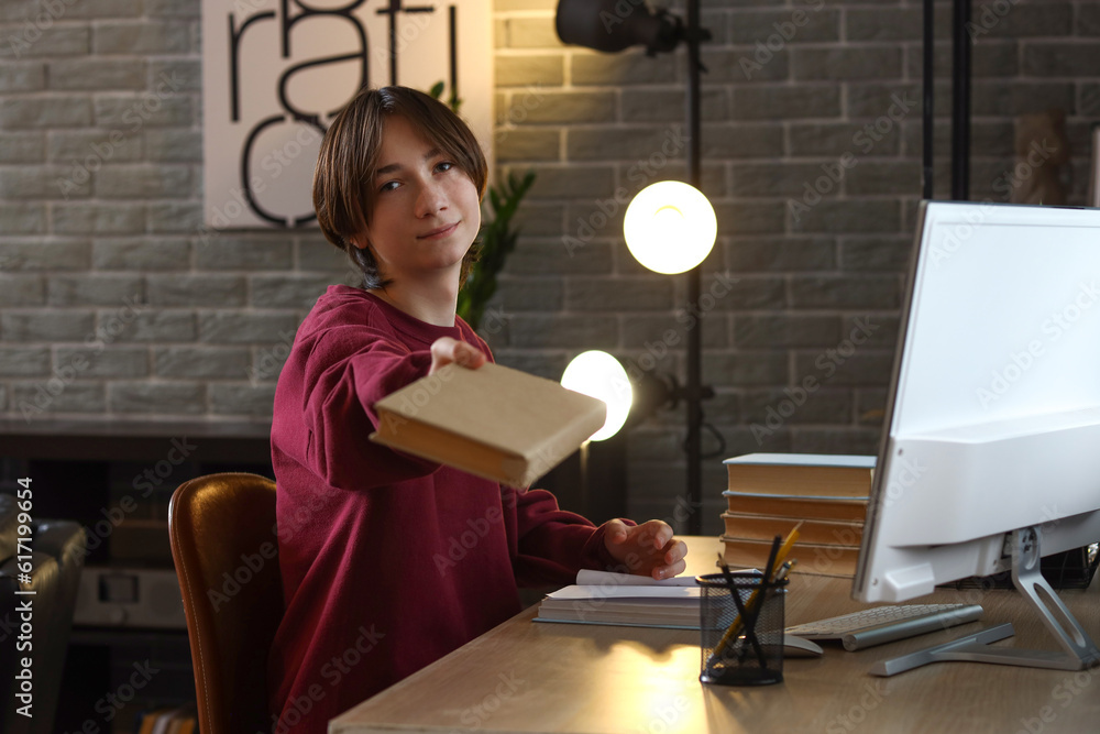 Teenage boy with book sitting at table late in evening