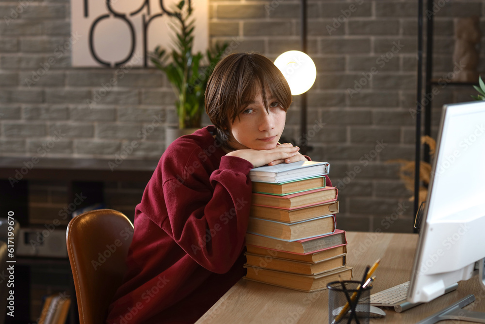 Teenage boy with stack of books on table late in evening