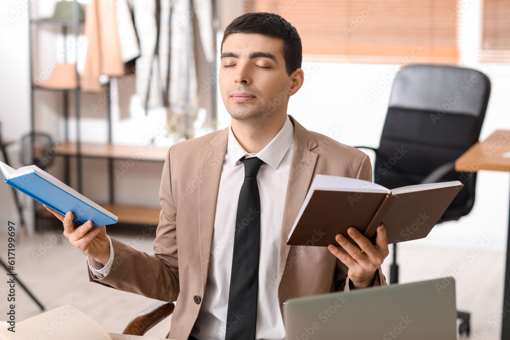 Young businessman with books meditating in office. Balance concept