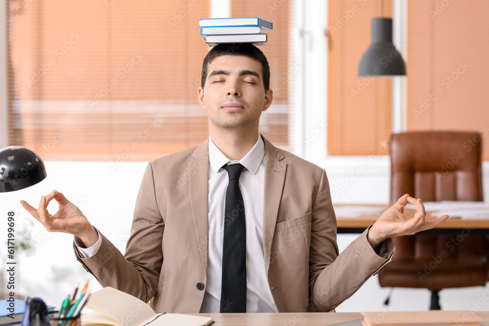 Young businessman with books meditating in office. Balance concept