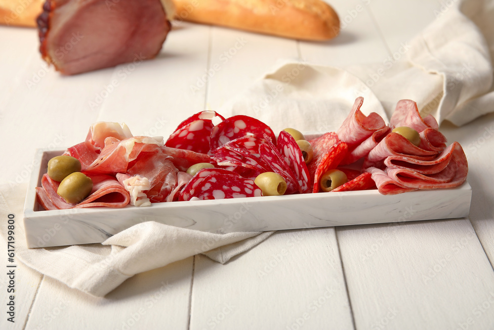 Plate with assortment of tasty deli meats on white wooden background