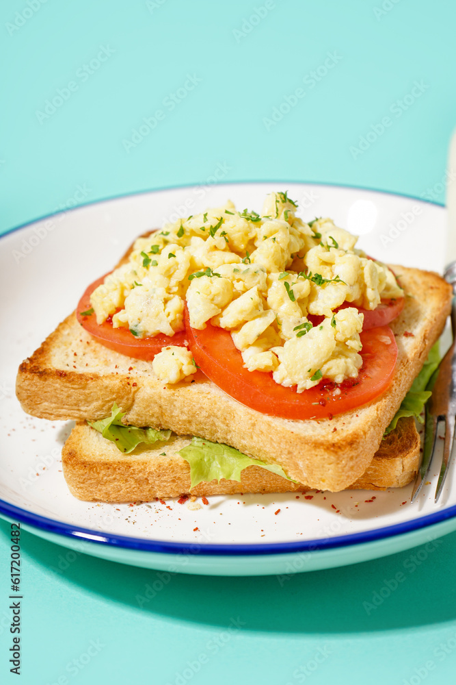 Plate with tasty scrambled eggs sandwich on blue background