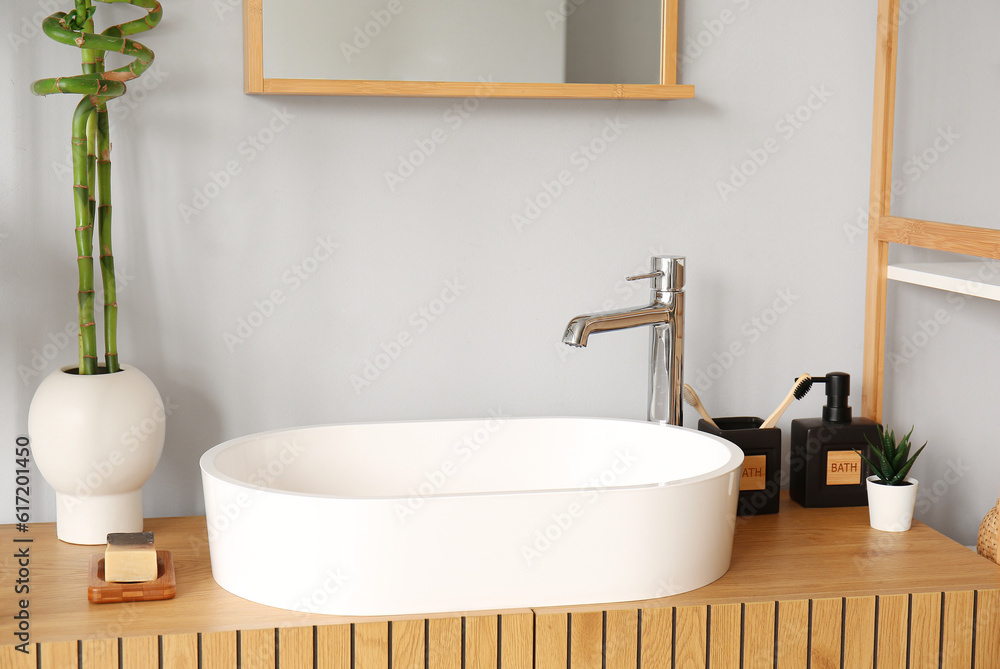 White sink, bath accessories and vase with bamboo stems on table in room