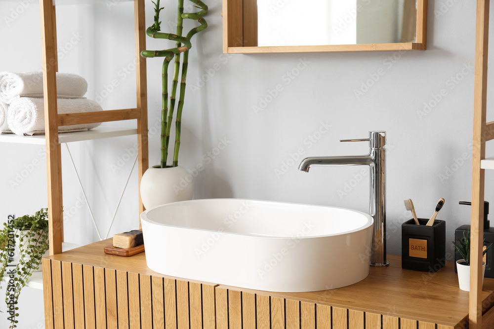 White sink, bath accessories and vase with bamboo stems on table in room