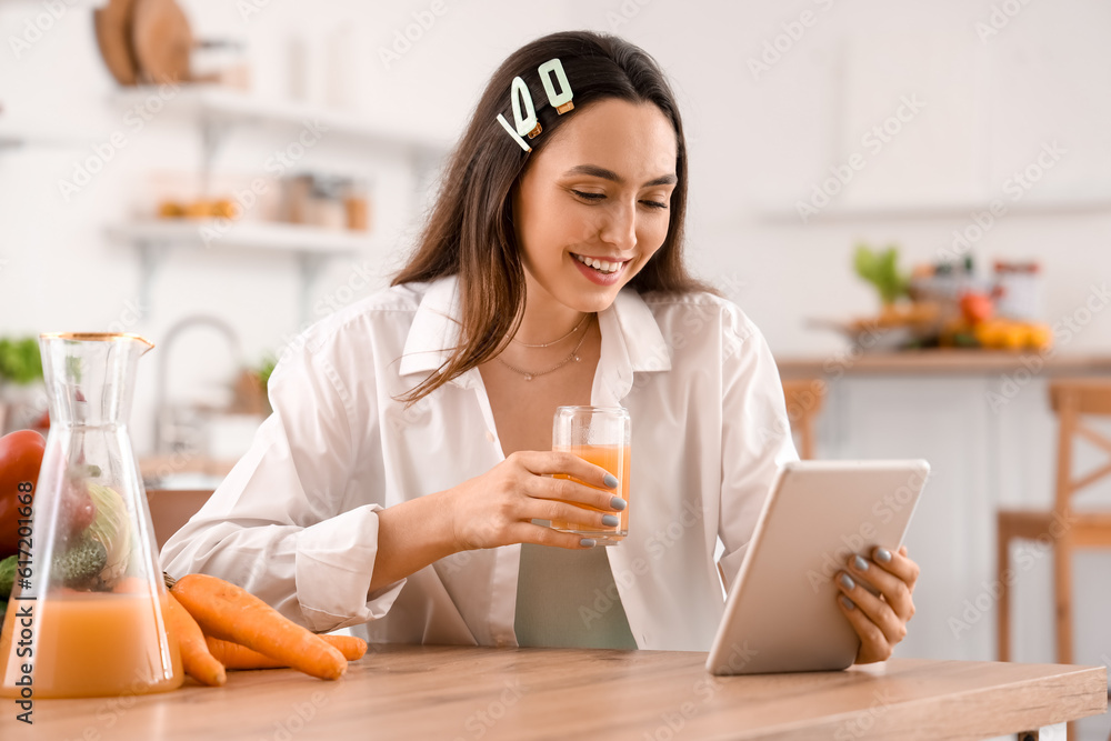 Young woman with glass of vegetable juice using tablet computer in kitchen