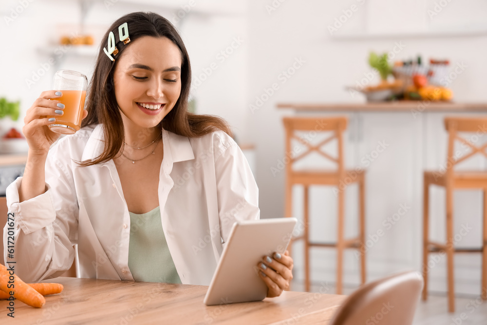 Young woman with glass of vegetable juice using tablet computer in kitchen