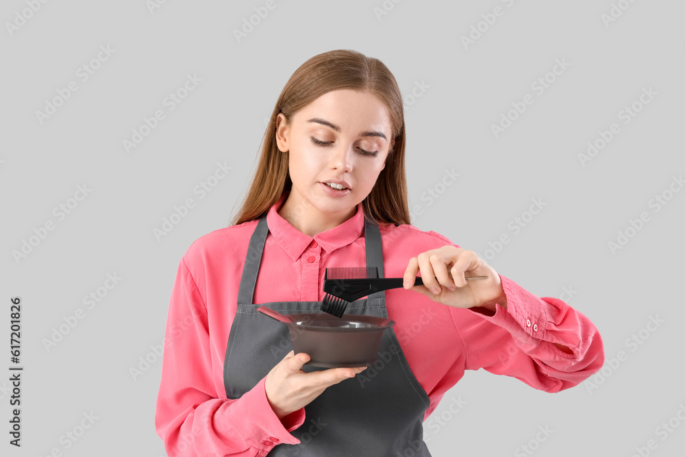 Female hairdresser with bowl and brush for hair dye on grey background