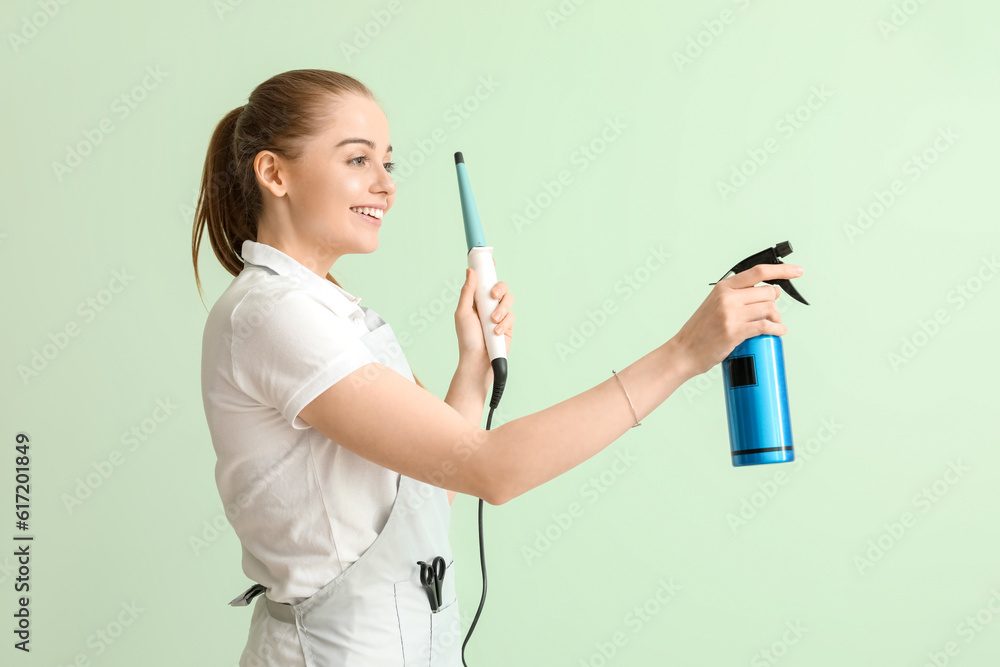 Female hairdresser with curling iron and spray on green background