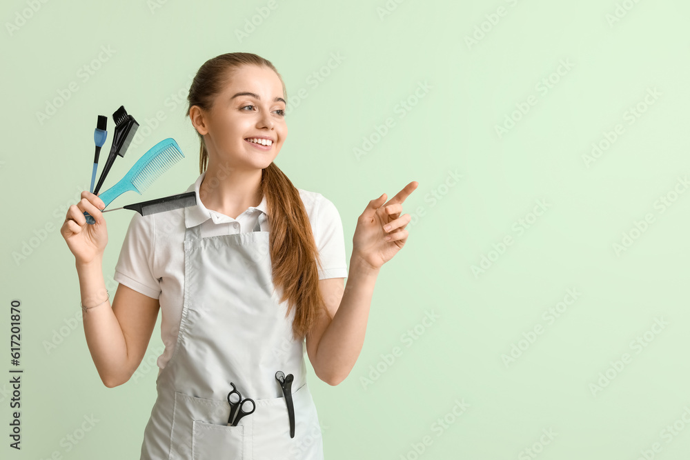 Female hairdresser with brushes pointing at something on green background