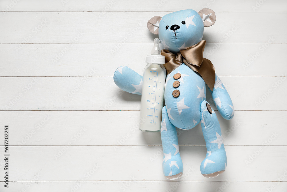 Teddy bear with bottle of milk for baby on white wooden background