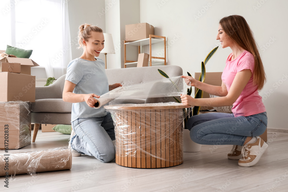 Young women wrapping coffee table with stretch film at home