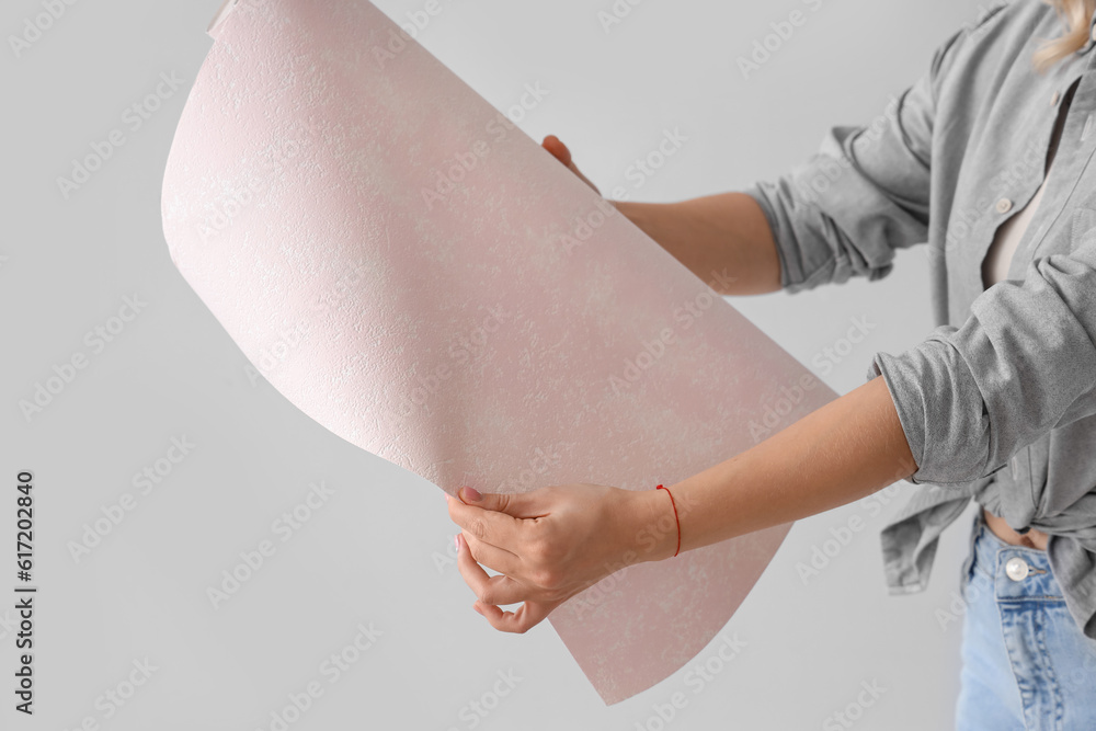 Young woman with wallpaper roll on grey background, closeup