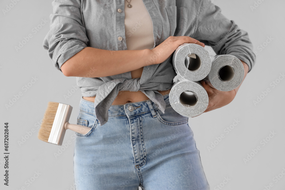 Young woman with wallpaper rolls on grey background, closeup