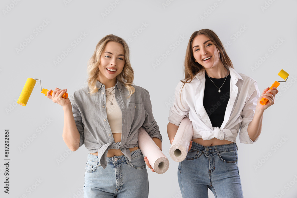 Young women with wallpapers and rollers on grey background