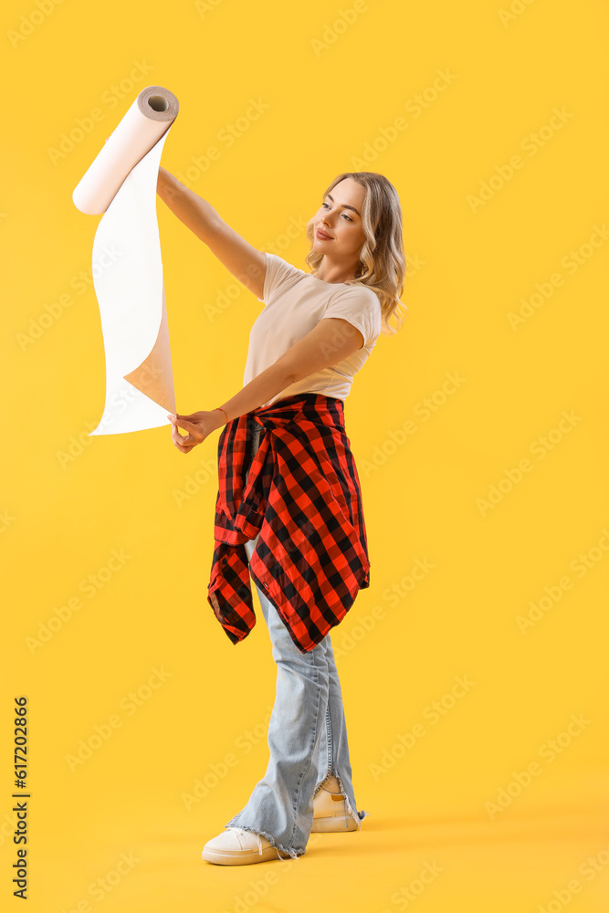 Young woman with wallpaper roll on yellow background