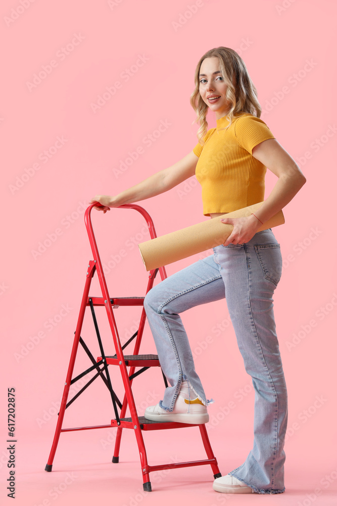 Young woman with wallpaper roll and ladder on pink background