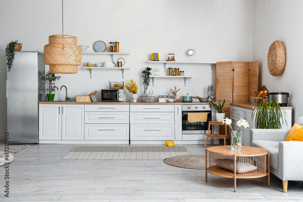 Interior of light kitchen with stylish fridge, counters, shelves, sofa and lamp