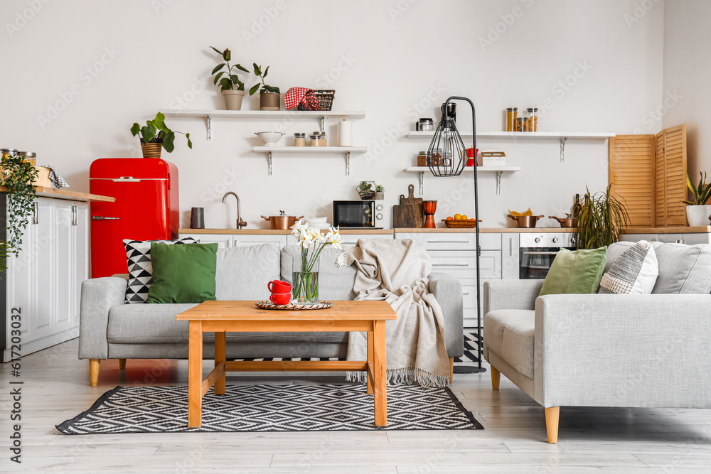 Interior of light kitchen with red fridge, counters, shelves, table and sofas