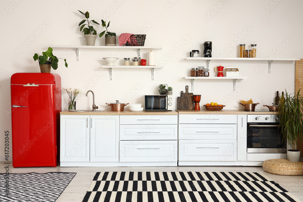 Interior of light kitchen with red fridge, counters, shelves and houseplants