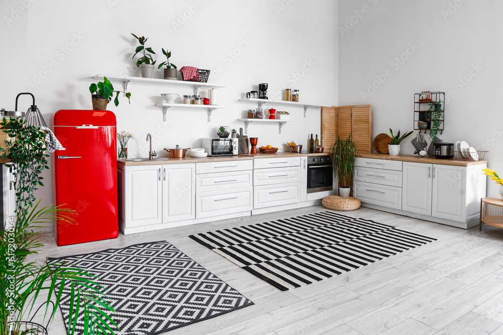 Interior of light kitchen with red fridge, counters, shelves and houseplants