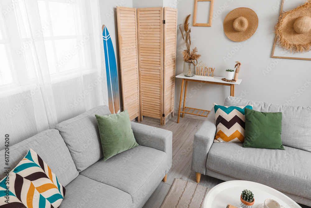 Interior of light living room with surfboard, table and sofas