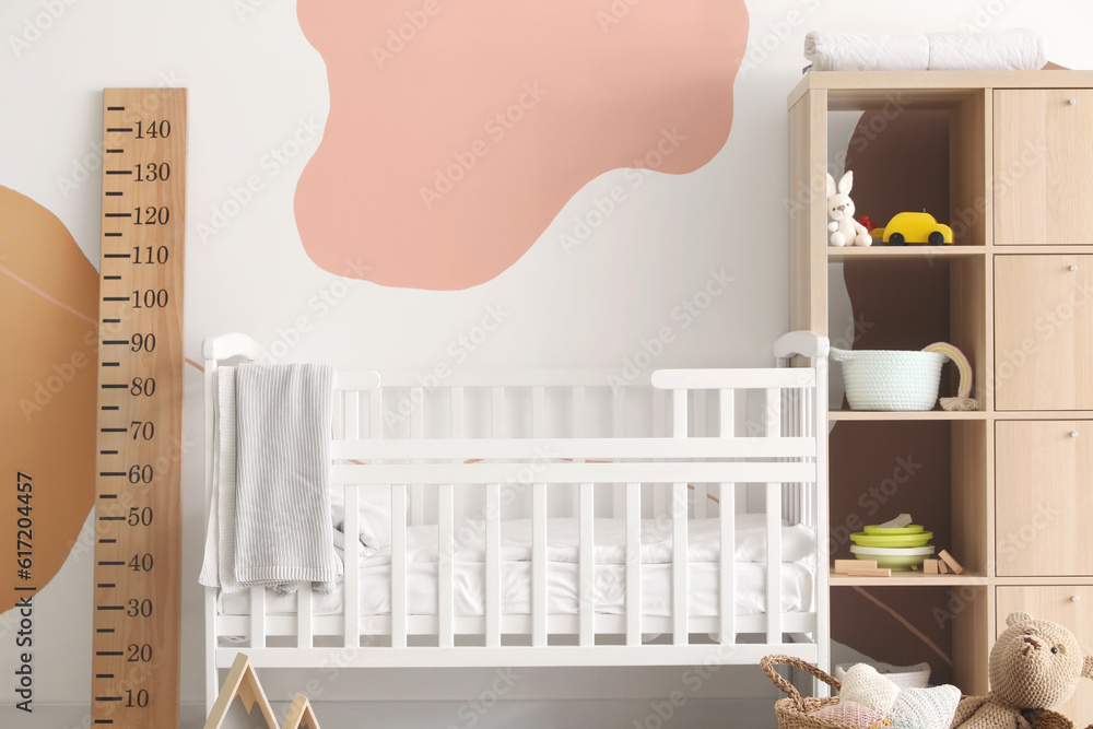 Interior of childrens bedroom with crib, stadiometer and shelving unit