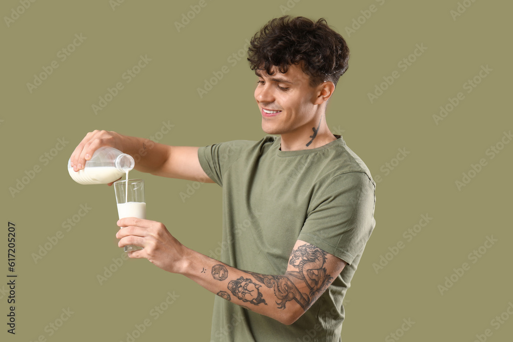 Young man pouring milk into glass on green background